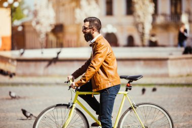 Yakışıklı genç sakallı adam uzakta onun bisiklet açık havada üzerinde sürme sırasında seyir güneş gözlüğü yan görünüm.