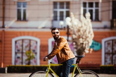 Sakallı yakışıklı genç güneş gözlüğü binmek bisiklet üzerinde güneşli şehir sokak