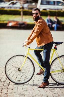 Genç gözlük ayarlama ve Onun Bisiklet açık havada üzerinde otururken kameraya bakarak adam sakallı