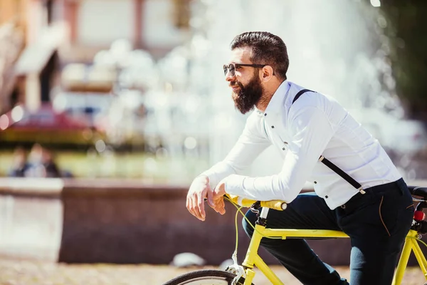 Retrato de belo jovem barbudo apoiado em sua bicicleta enquanto estava em fontes ao ar livre — Fotografia de Stock