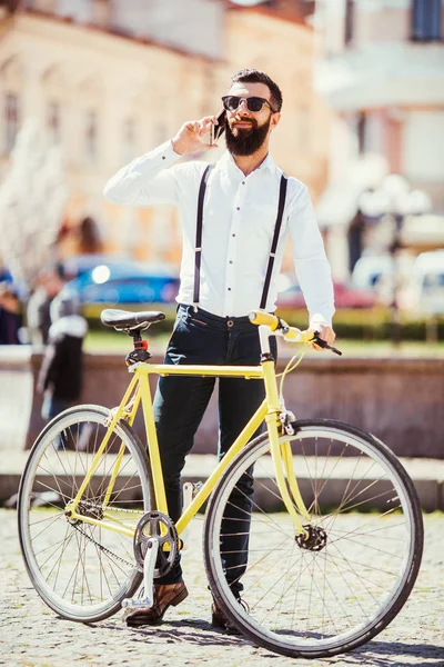 Homem barba alegre com barba falando no telefone celular e sorrindo enquanto estava perto de sua bicicleta . — Fotografia de Stock