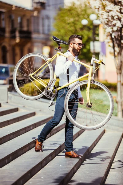 Homem barbudo com bicicleta fixa. Vista de confiante jovem barbudo carregando sua bicicleta no ombro e olhando para longe enquanto caminhava ao ar livre nas escadas da cidade — Fotografia de Stock