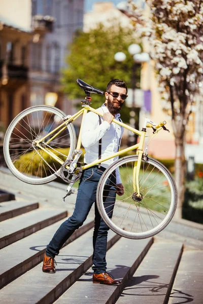 Hipster-Mann mit Sonnenbrille, der sein Schulterfahrrad auf der Treppe trägt. ein junger gutaussehender Mann mit Bart und Fahrrad am rechten Arm. — Stockfoto