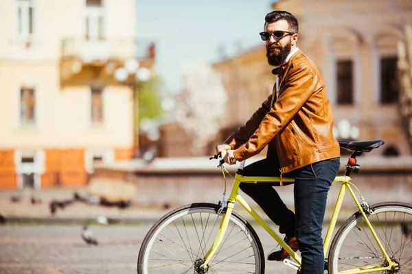 Zijaanzicht van de knappe jonge bebaarde man in zonnebril op zoek weg tijdens het rijden op zijn fiets buitenshuis. — Stockfoto