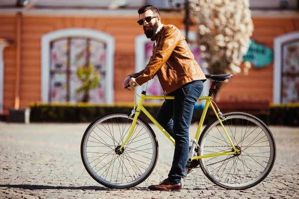 Красивый молодой бородатый мужчина в солнечных очках катается на велосипеде по солнечной улице. — стоковое фото