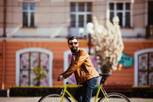 Bonito jovem barbudo em óculos de sol andar de bicicleta na ensolarada rua da cidade — Fotografia de Stock