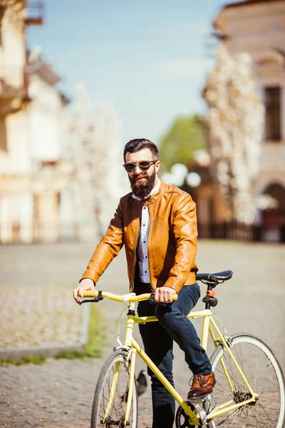 Bonito jovem barbudo de óculos de sol de bicicleta na cidade. Conceito de bicicleta — Fotografia de Stock