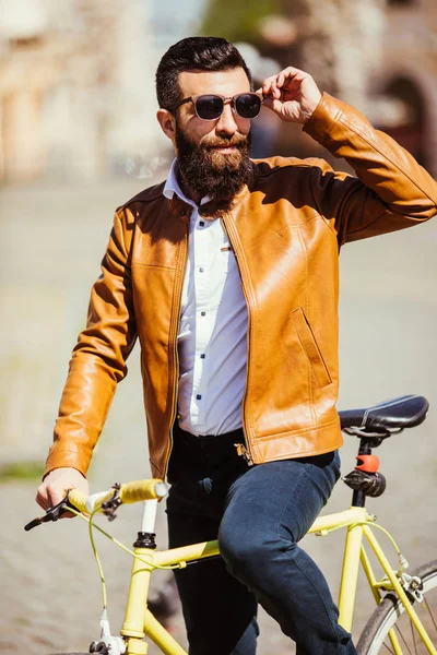 Bonito jovem barbudo de óculos de sol de bicicleta na cidade. Conceito de bicicleta — Fotografia de Stock