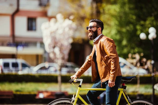 Homem barbudo jovem ajustando óculos e olhando para a câmera enquanto sentado em sua bicicleta ao ar livre — Fotografia de Stock