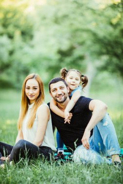 Genç aile anne baba ve çim parkta oturan kız