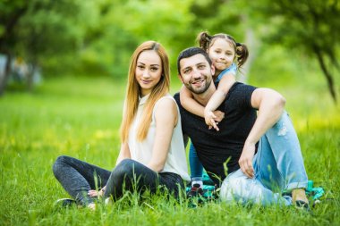 Mutluluk ve uyum içinde aile hayatı. Mutlu aile kavramı. Genç anne ve babası ile kızları parkta. Mutlu bir aile birlikte yeşil çimenlerin üzerinde dinlenme. Aile açık eğleniyor