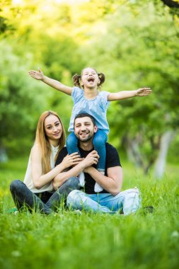 Üç birlikte eğleniyor genç mutlu aile açık. Küçük kızı babası üzerine gülümseyen omzunda ve iyi eğlenceler.