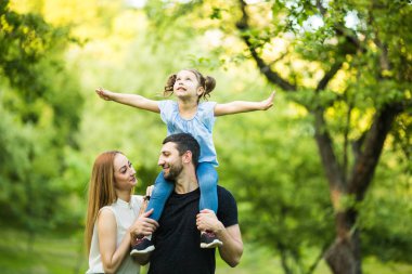 Baba, anne ve genç kızı sırtlama yaz park arka plan üzerinde uçan gibi kaldırdı elleriyle üzerine