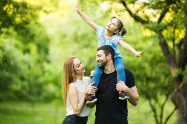 Baba, anne ve genç kızı sırtlama yaz park arka plan üzerinde uçan gibi kaldırdı elleriyle üzerine