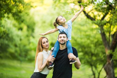 Üç birlikte eğleniyor genç mutlu aile açık. Küçük kızı baba sırtında. Aile eğlencesi dışında.