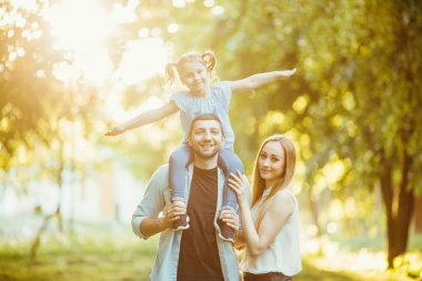 Doğa geç öğleden sonra güneş ışığında yaz sonbaharda oynarken mutlu bir aile. Anne, baba ve kız parkta, gülen ve gülümseyen, eğlenceli, çimlerin üzerine sevinç oynamak.