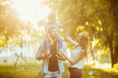 Doğa geç öğleden sonra güneş ışığında yaz sonbaharda oynarken mutlu bir aile. Anne, baba ve kız parkta, gülen ve gülümseyen, eğlenceli, çimlerin üzerine sevinç oynamak.
