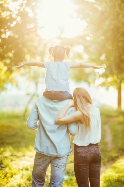Mutlu aile üç kişinin çim sunset bulvarında Park'ta yürüyordunuz. mutlu kızı babası sırt üstü uçan