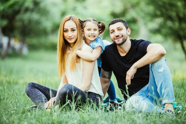 Bonheur et harmonie dans la vie familiale. Joyeux concept de famille. Jeune père et mère avec leur fille dans le parc. Joyeux famille reposant ensemble sur l'herbe verte. Famille s'amuser en plein air — Photo