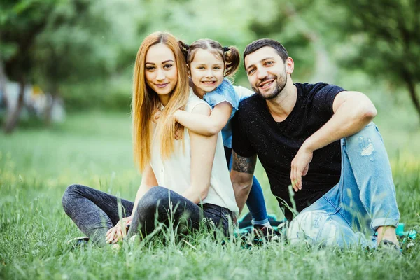 Jeune famille heureuse dans le parc d'été. Père et mère passent du temps dans le parc d'été avec leur fille pendant qu'elle les étreint . — Photo