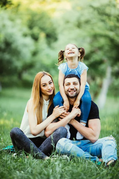Happy mother, father and daughter in the park. Beauty nature scene with family outdoor lifestyle. Happy daughter on father back smile.