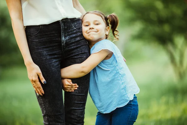 Madre e hija divirtiéndose en el parque. Hija abrazo madre pierna aginst verano fondo — Foto de Stock