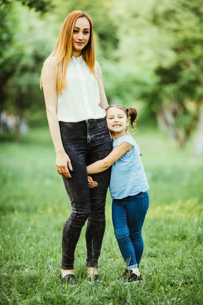 Madre e hija divirtiéndose en el parque. Hija abrazo madre pierna aginst verano fondo — Foto de Stock