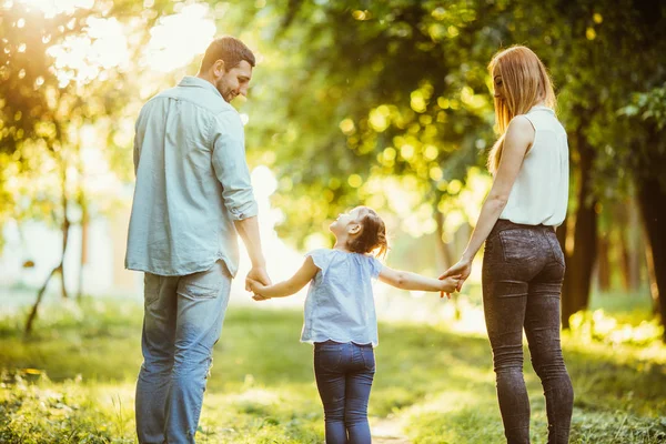 Gelukkige familie in het park. Moeder, vader en baby gelukkig lopen bij zonsondergang. Het concept van een gelukkige familie. Ouders van de baby handen te houden. — Stockfoto