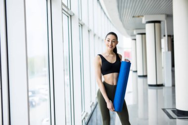 Yoga mat olan mutlu kadın fitness panoramik pencerelere arka plan üzerinde hazırdır