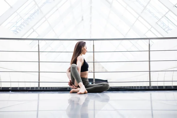 Vackra yoga kvinnan praxis i en bakgrund med stora fönster i hallen. Yoga-konceptet. — Stockfoto