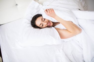 Güzel esmer kadın beyaz yatak çarşafları yumuşak sabah hafif yatıyor. Mutlu aile yaşam, gevşeme, konfor, eğlenceli kavramı. Üstten Görünüm.