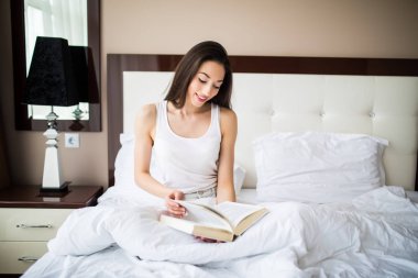 bir kitap okuma ve o yatakta oturur gibi gülümseyen kadın.