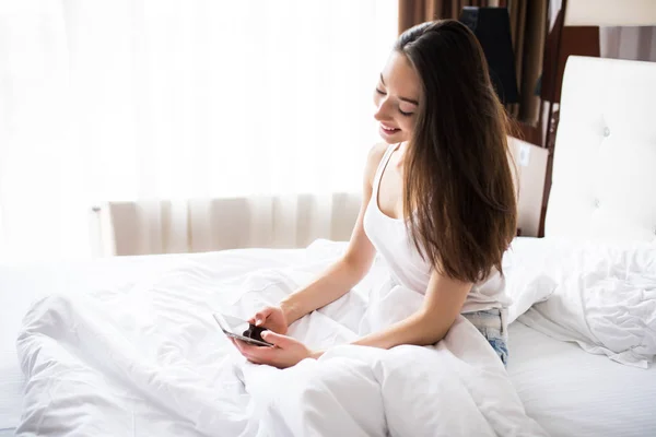 Женщина, лежащая в постели, тянется, чтобы проверить мобильный телефон утром — стоковое фото