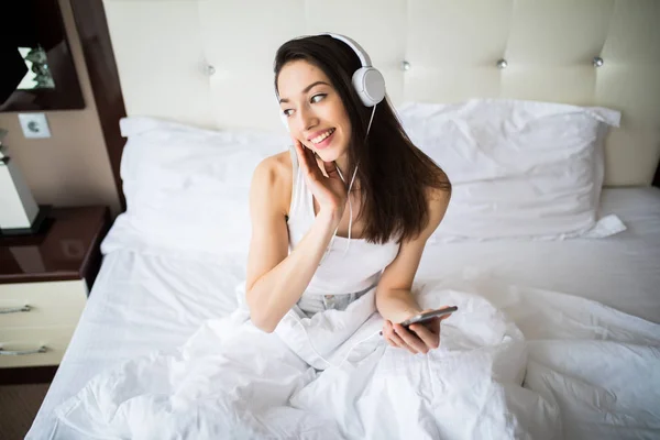 幸せな女またはスマート フォンから音楽を聴くと、自宅のベッドの上でダンスのヘッドフォンで十代の少女 — ストック写真