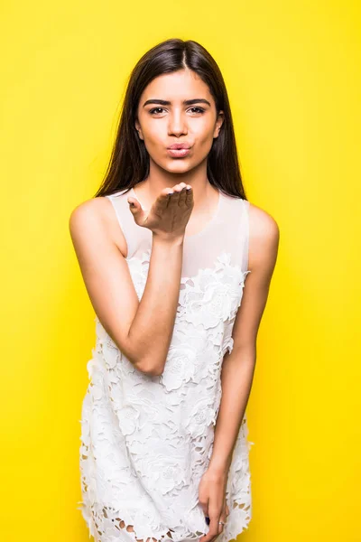 Krásná mladá žena odeslat vzduch polibky na žlutou barvu pozadí — Stock fotografie