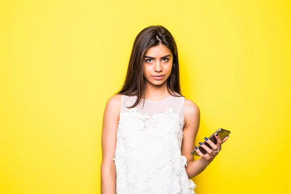 Rester connecté. Joyeux jeune femme regardant son téléphone mobile isolé fond de mur jaune . — Photo