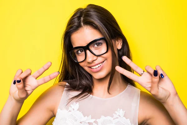 Young girl wearing eyeglasses with victory gesture in yellow background. Girl looking at camera. — Stock Photo, Image