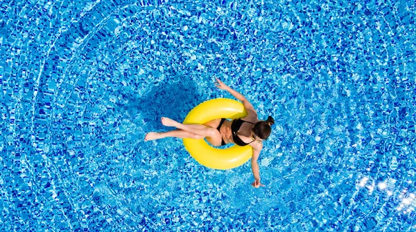 Luchtfoto van jonge brunette vrouw op de opblaasbare grote gele in het zwembad zwemmen. Bovenaanzicht van slanke dame ontspannen op haar vakantie. — Stockfoto