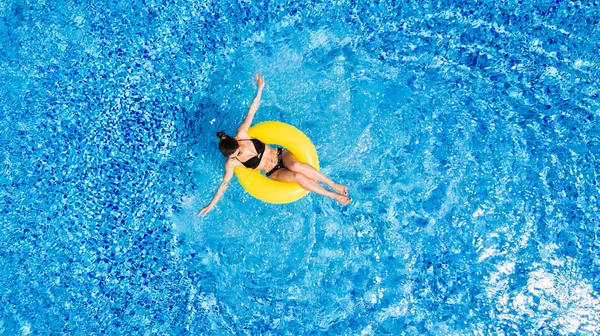 Ferienkonzept. Draufsicht auf die schlanke junge Frau im Bikini auf dem gelben Luftaufblasring im großen Schwimmbad. — Stockfoto
