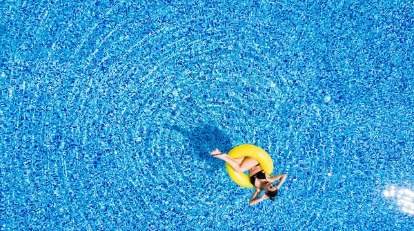 Повітряний вид на молоду брюнетку, що плаває на надувному великому жовтому кільці в басейні — стокове фото