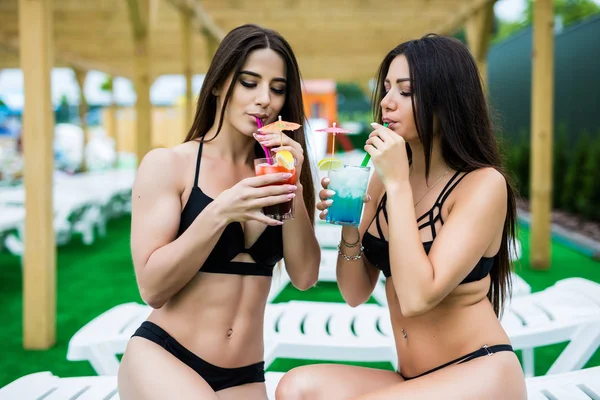 Pozwól rozpocząć wakacje. Dwie piękne kobiety razem mając koktajle przy basenie — Zdjęcie stockowe
