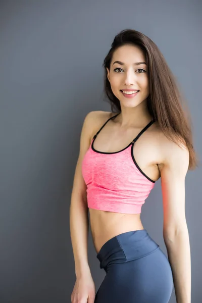 Schöne Fitness-Frau steht isoliert vor grauem Hintergrund — Stockfoto