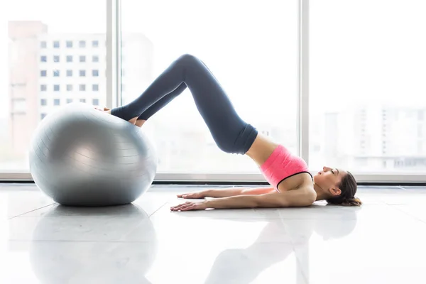 Mulher e bola de fitness. Jovem fazendo exercícios com bola em forma no ginásio. Mulher está fazendo fitness em casa no chão da sala perto da janela . — Fotografia de Stock