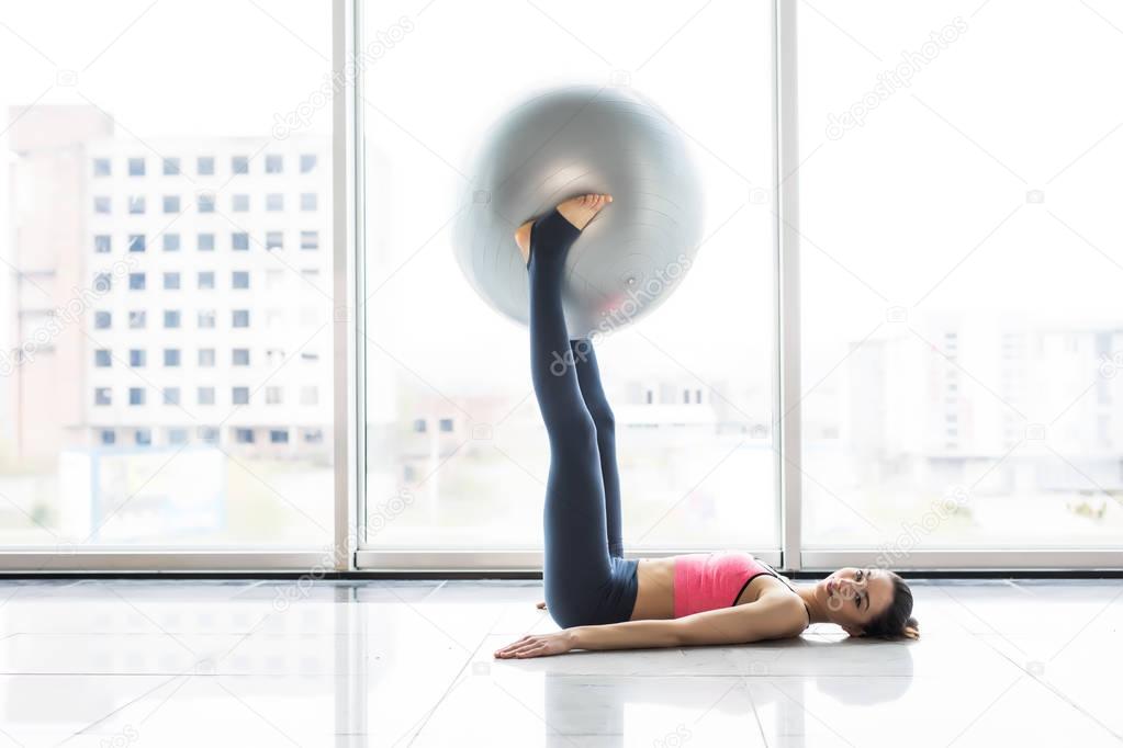 Woman working out with exercise ball in gym. Pilates woman doing exercises in the gym workout room with fitness ball. Fitness woman doing exercises for muscle press with abs swiss ball.