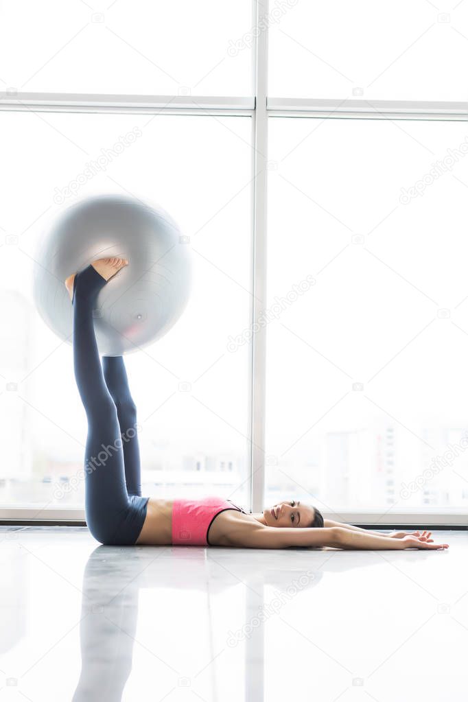 Woman working out with exercise ball in gym. Pilates woman doing exercises in the gym workout room with fitness ball. Fitness woman doing exercises for muscle press with abs swiss ball.