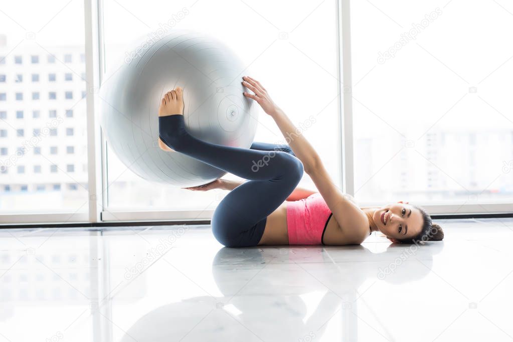 Woman working out with exercise ball in gym. Pilates woman doing exercises in the gym workout room with fitness ball. Fitness woman doing exercises for muscle press with abs swiss ball.