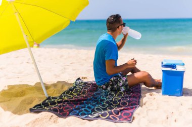 Yeşil güneş şemsiyesi içecek su soğutucu plajda altında genç adam