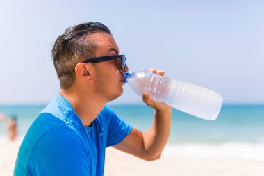 Yeşil güneş şemsiyesi içecek su soğutucu plajda altında genç adam