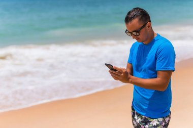 Adam telefonu beach yazarak üzerinde veya Internet güneşli günde kullanın