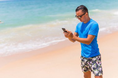 Adam telefonu beach yazarak üzerinde veya Internet güneşli günde kullanın